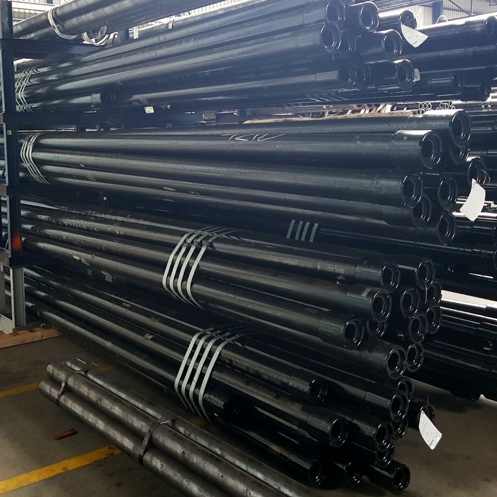 Stacks of black metal pipes arranged on shelves in a warehouse with a high ceiling and metal beams.